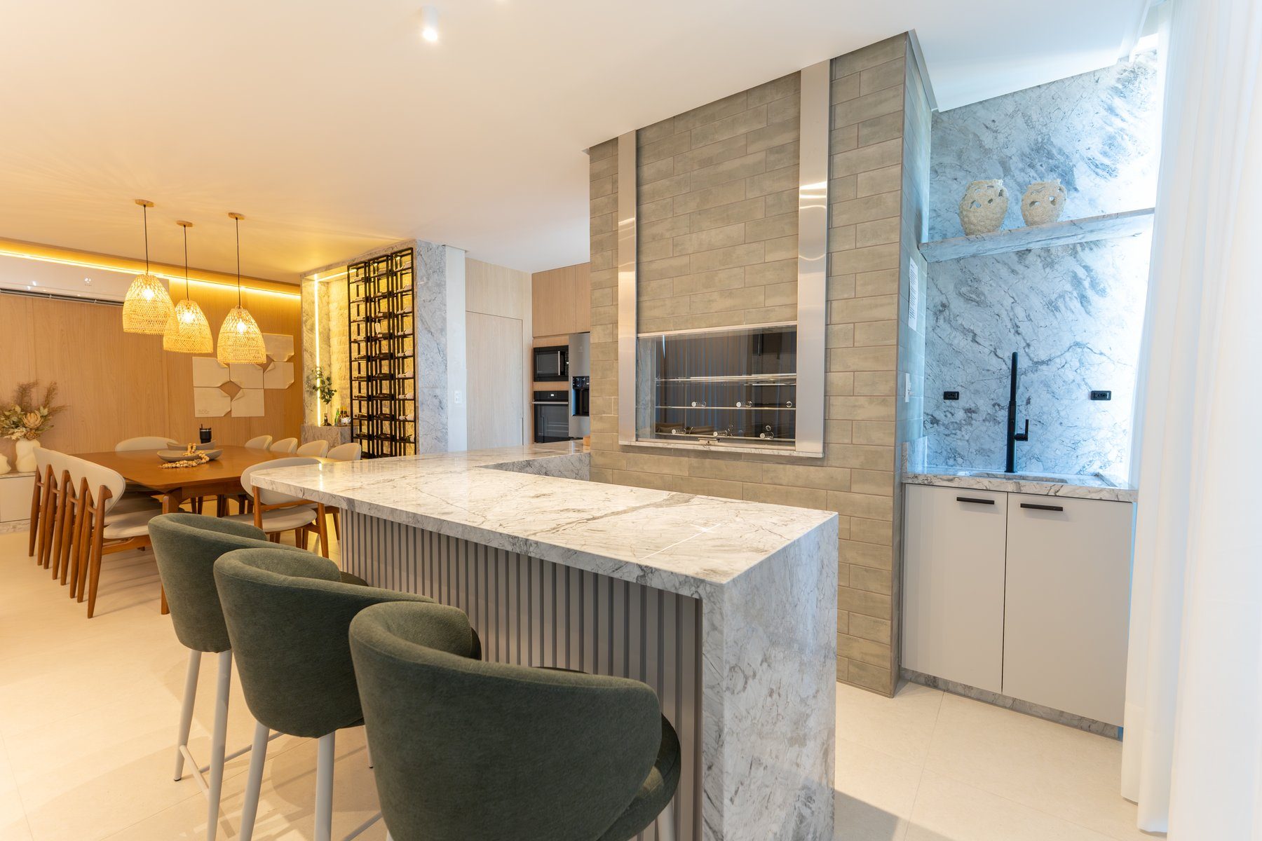 Bancada gourmet em mármore com banquetas verdes, adega de vinhos e cozinha integrada à sala de jantar